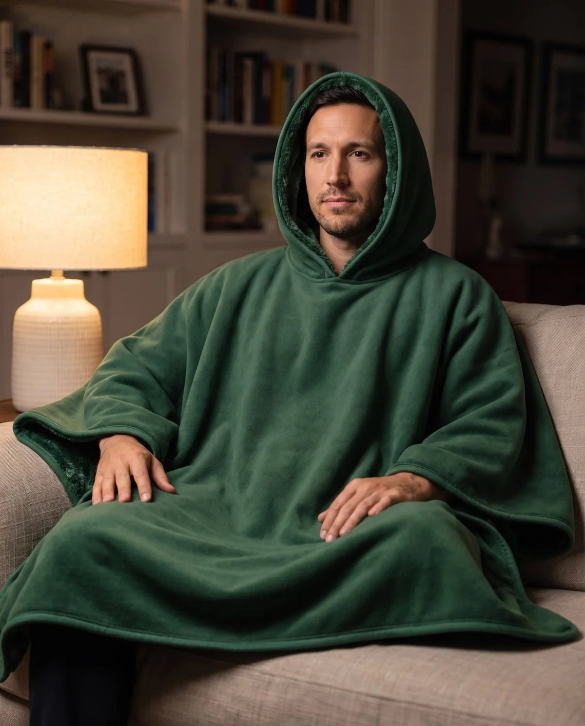 Man watching television in the evening wearing the Hazel hooded blanket in forest green with the hood up