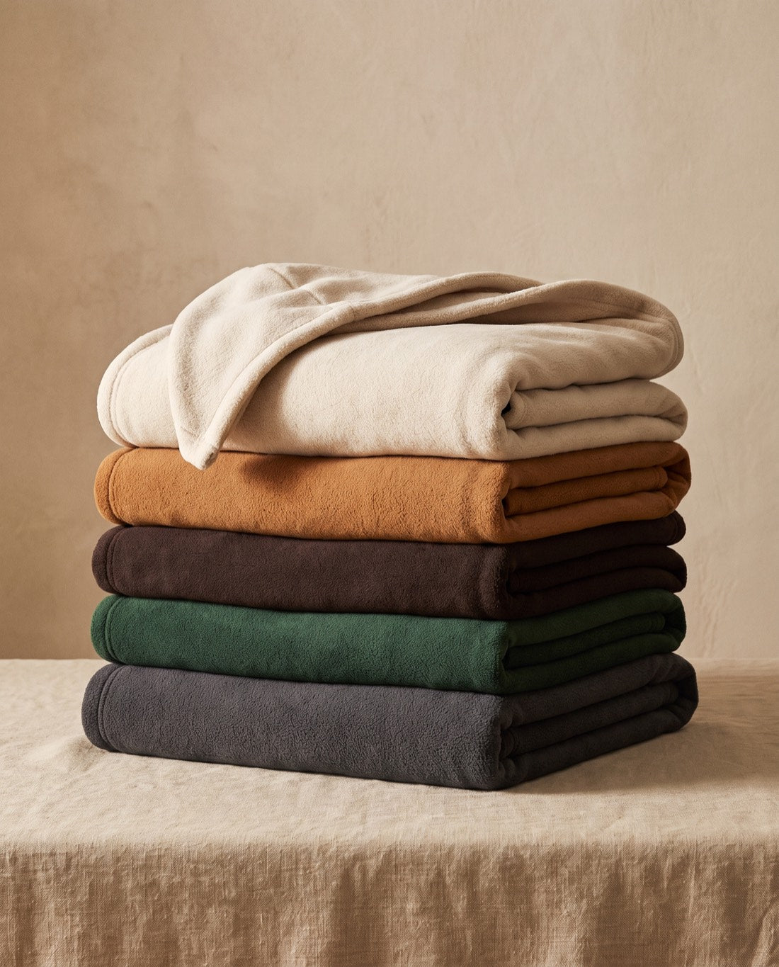 Five folded Alle Boutique hooded blankets stacked in oatmeal, cognac, espresso, forest green and charcoal