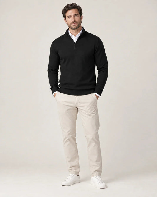 Ansel men's half-zip sweater in black with a stand collar and ribbed cuffs and hem, worn over a white shirt with beige chinos, front view on a model
