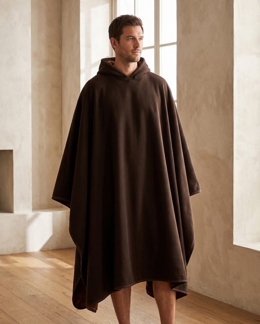 Man wearing the Otis oversized hooded blanket in deep espresso, standing in a warm living room, front view